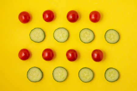 Pattern of red tomatoes and green cucumber slices on a bright yellow background. Vegans concept. Suitable for posters and packaging. Flat lay style, top viewの写真素材
