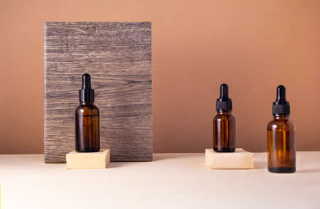Set of glass bottles on wooden podiums for serum on beige background. Cosmetic product decorated with ceramic material with wood texture and pattern. Liquid skin or hair care product. Front viewの写真素材