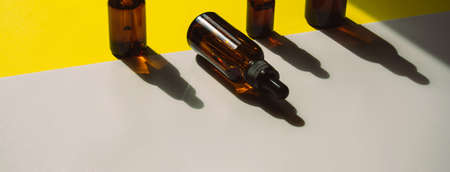 A set of bottles for cosmetic products on a yellow-white background. The containers are standing, and the shadow falls on the background. One bottle lies on the surface. Hard light. Bannerの写真素材