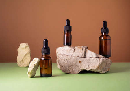 Serum and oil cosmetic bottles on concrete stone podium on brown and green background. Trendy natural organic healthy hair, face and body skin careの写真素材