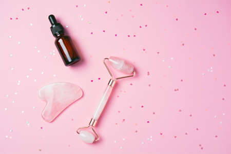 Roller and gua sha massage scraper and beauty product on a pink background with sparkles in the shape of hearts. Serum or oil and skincare tools. Wellness concept. Copy spaceの写真素材