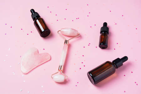 Roller and gua sha massage scraper and beauty products on a pink background with sparkles in the shape of hearts. Serum or oil and skincare tools. Wellness concept. Copy spaceの写真素材