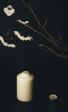 Halloween decoration, ghosts and paper bats, candle, tree branches on a black background. Backdrop for holiday and party, copy spaceの写真素材