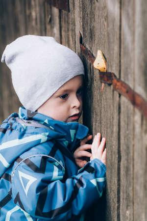 A child peeks through a wooden fence. Curious, inquisitive boy exploresの写真素材