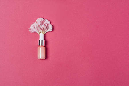Serum in a pink bottle with carnation petals on a pink background. Aromatherapy oil, natural cosmetics concept. Minimalism. Top view, copy spaceの写真素材