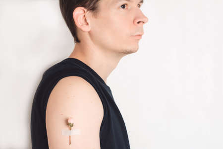 A man with a flower under a patch on his shoulder looks to the side, into a future healthy life. COVID-19 immunization concept. Copy spaceの写真素材