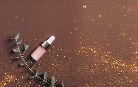 Serum in a pink bottle on a brown background with sparkle. Aromatherapy oil, natural cosmetics concept and festive view. Top view, copy spaceの写真素材