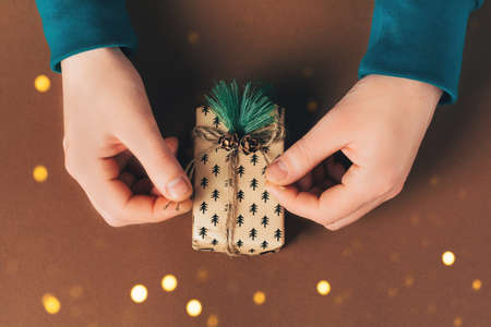 Male hands are packing a gift box on the eve of holidays Christmas and New Year on brown background. Eco-friendly concept, zero waste christmas.の写真素材