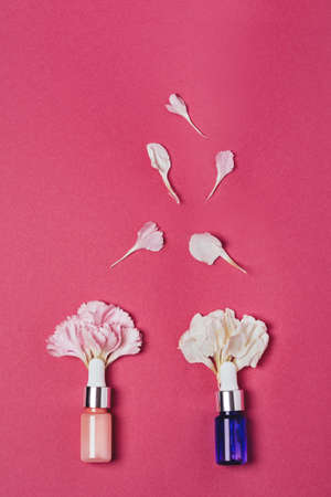 Serum in a pink and purple bottles with carnation petals on a pink background. Aromatherapy oil, natural cosmetics concept. Top view, verticalの写真素材