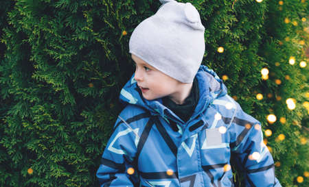 Child peeking out from behind a tree with golden lights outdoorsの写真素材