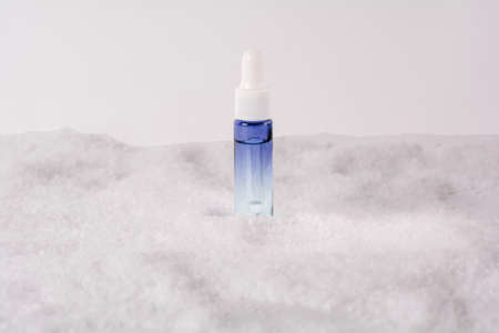 Serum glass bottle in the snow. Liquid skin or hair care product. Christmas and holiday concept. Front view and copy spaceの写真素材