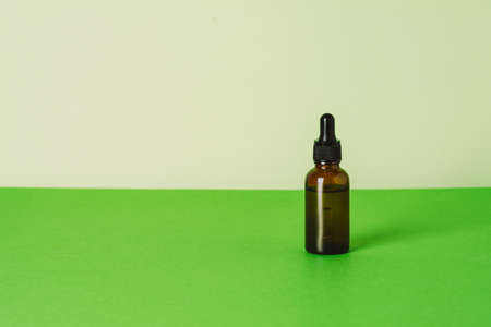 Serum glass bottle on green background. Liquid skin or hair care product. Natural cosmetics concept. Front view, copy spaceの写真素材