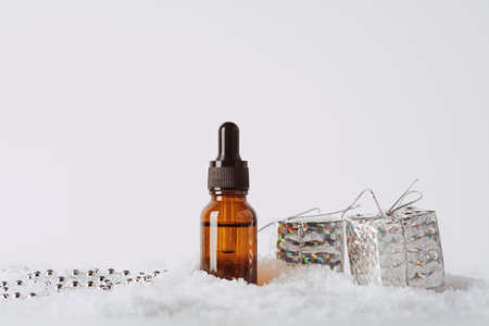 Serum glass bottle in the snow with christmas decoration: gift boxes on a white background. Liquid skin or hair care product. Front viewの写真素材