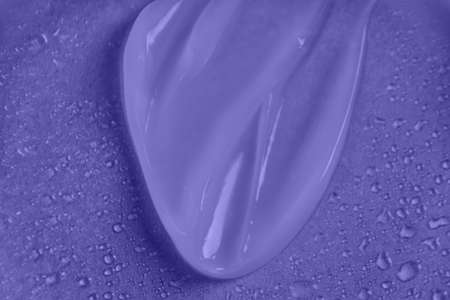 Liquid cosmetic product on purple background with water drops