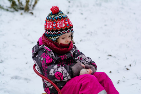 Pensive child sitting on sledging, winter activities for childrenの写真素材