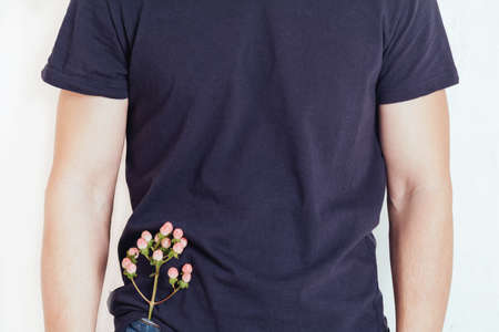 A man in a T-shirt with a flower in his jeans pocket on a white background. Health, wellness and environmental care concept. Copy spaceの写真素材