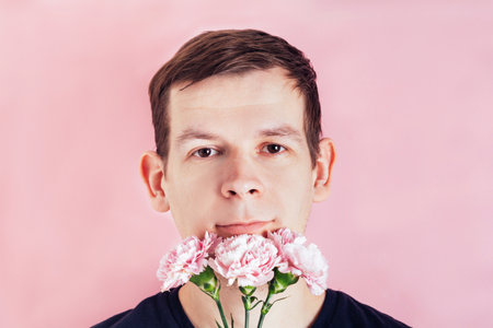 Portrait of a man with flowers near his face on a pink background. Birthday, mother's or valentine's day giftの写真素材