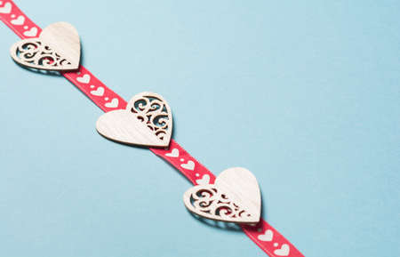 Wooden hearts with a red ribbon in white hearts on a blue background. Background for the holiday of Valentine's Day. The concept of love, romance and tendernessの写真素材