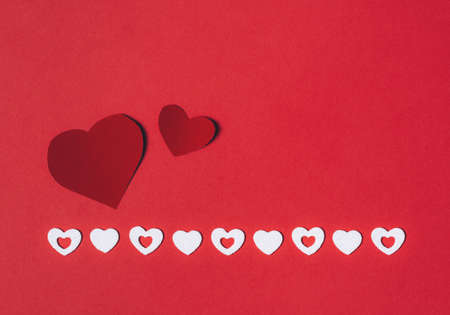 Red paper hearts and shiny white hearts on a red background. Background for the holiday of...