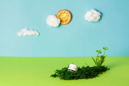 Facial cosmetic product on blue background with cotton wool clouds, orange sun and green plants. Eco...
