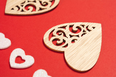 Close-up of wooden hearts and shiny white hearts on a red background. Background for the holiday of Valentine's Day. The concept of love, romance and tendernessの写真素材