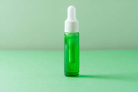 Facial liquid cosmetic product with bubbles on green background. Front view, copy spaceの写真素材