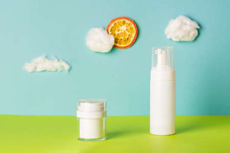 Set of cosmetic products on blue background with cotton wool clouds and orange sun. Eco and natural beauty concept. Art and trend. Front view, copy spaceの写真素材