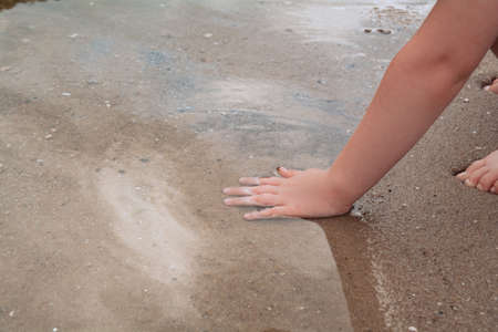 The child dips his hand into the water and tries the sand. The concept of freedom, natural and wellbeingの写真素材