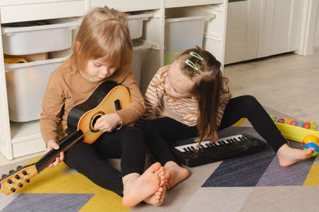 Happy children playing musical instruments at home. Sisters have fun in the roomの写真素材