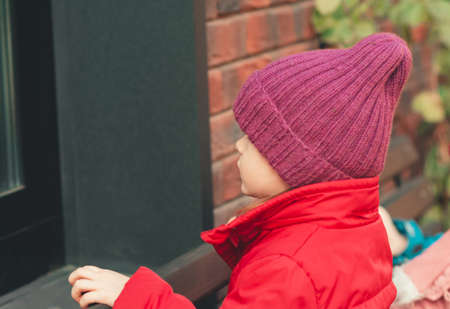 A small child looks out the window from the street. The boy sees his reflection in the mirror windowの写真素材