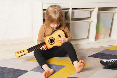 Child at home learning to play the guitar. Leisure and education at home. child portrait looking at the guitarの写真素材