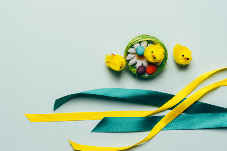 Easter composition with decorative yellow chickens and eggs in the nest with ribbons. Background for...