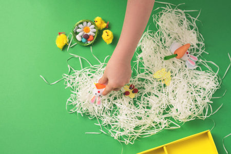 Children's hands arrange decorative decorations for easter: rabbits, chickens, carrots, a nest with...