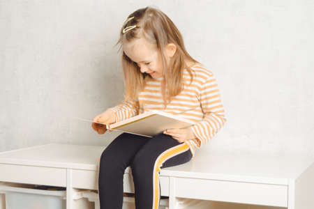 Cute child sitting on the closet and studying a book at home. Leisure and education at home. child portrait looking into a bookの写真素材