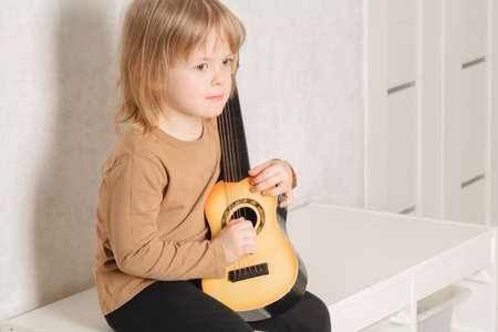 Child at home learning to play the guitar. Leisure and education at home. child portrait looking at...