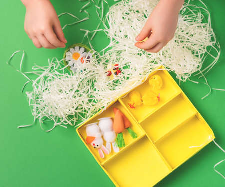 Children's hands arrange decorative decorations for easter: rabbits, chickens, carrots, a nest with...