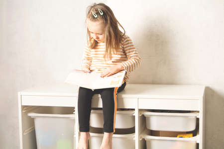 Cute child sitting on the closet and studying a book at home. Leisure and education at home. child portrait looking into a bookの写真素材