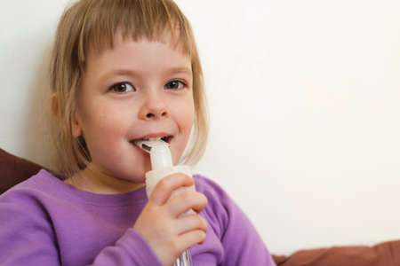Sick child lies in bed and makes inhalation using a nebulizer. Portrait of a smiling child with a nebulizer in his hand. Stage of recovery and restoration of immunityの写真素材