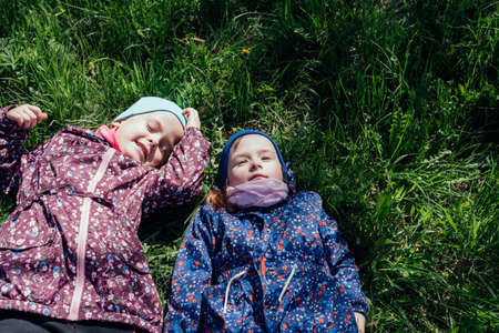 Two cute little girls lie on the fresh spring grass