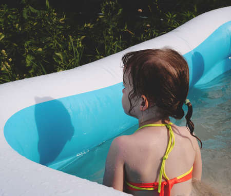 Child in the pool on a summer sunny day. Girl sits with his back, behind view. faceless trendの写真素材