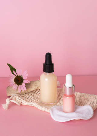 Cosmetic bottles with dropper for face and body skin care with extracts of flowers and plants with reusable cotton sponges for the face. Set of cosmetic bottles on a pink background. natural organic cosmetics. beauty conceptの写真素材