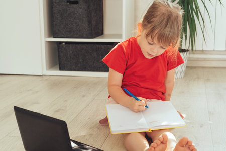 Cute girl is sitting on the floor with a laptop, a pen and a notepad.の写真素材