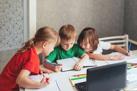 Children sit at a table with pens and notebooks and use a laptopの写真素材