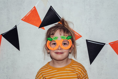 Portrait of a smiling girl in carnival glasses in the form of pumpkins. Happy child at home on halloween holidayの写真素材