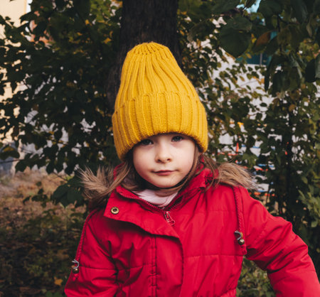 Portrait of a smiling girl in a red jacket and yellow hat