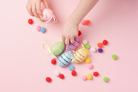 Children's hands collect Easter eggs on a pink background. Decorative eggs and fluffy balls on a pink background.の写真素材