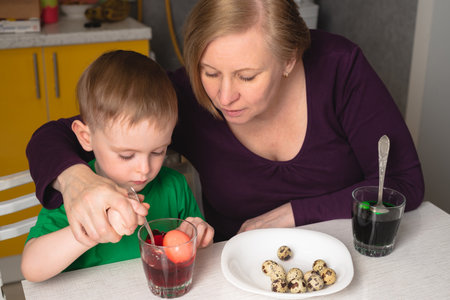 Grandmother helps her grandson paint Easter eggsの写真素材