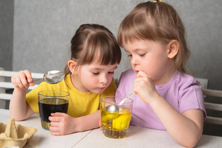 Children color eggs with food coloring. Sisters painting Easter eggs.の写真素材