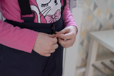 Close-up of hands that fasten a button on a jumpsuit. The child independently dresses for a walkの写真素材
