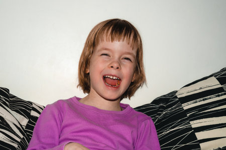 Girl sits on the sofa and eats dried apples. The child is laughing, happy and healthyの写真素材